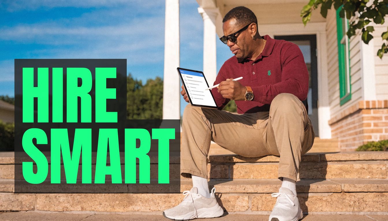 A man in a red shirt sitting on house steps, using a tablet to hire professionals.