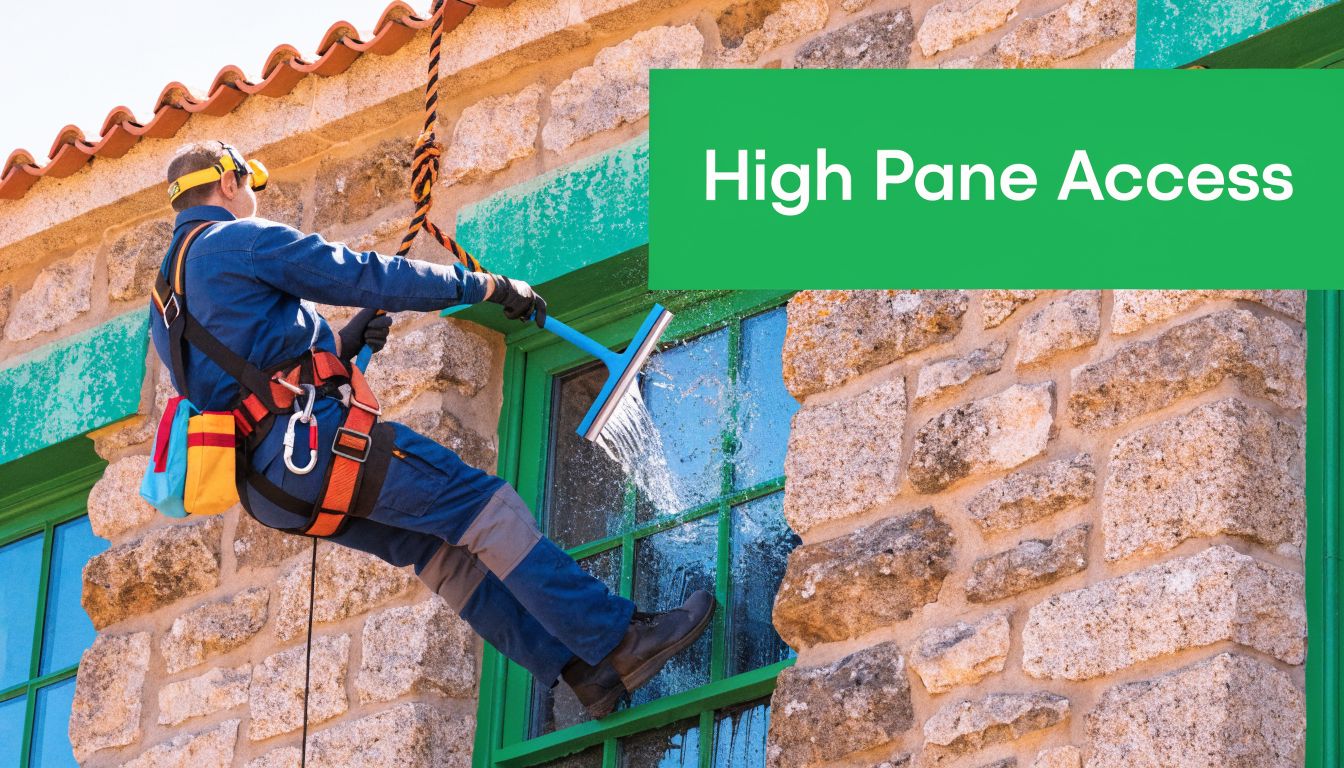 A professional window cleaner using a squeegee to clean a stone building window while suspended on ropes.