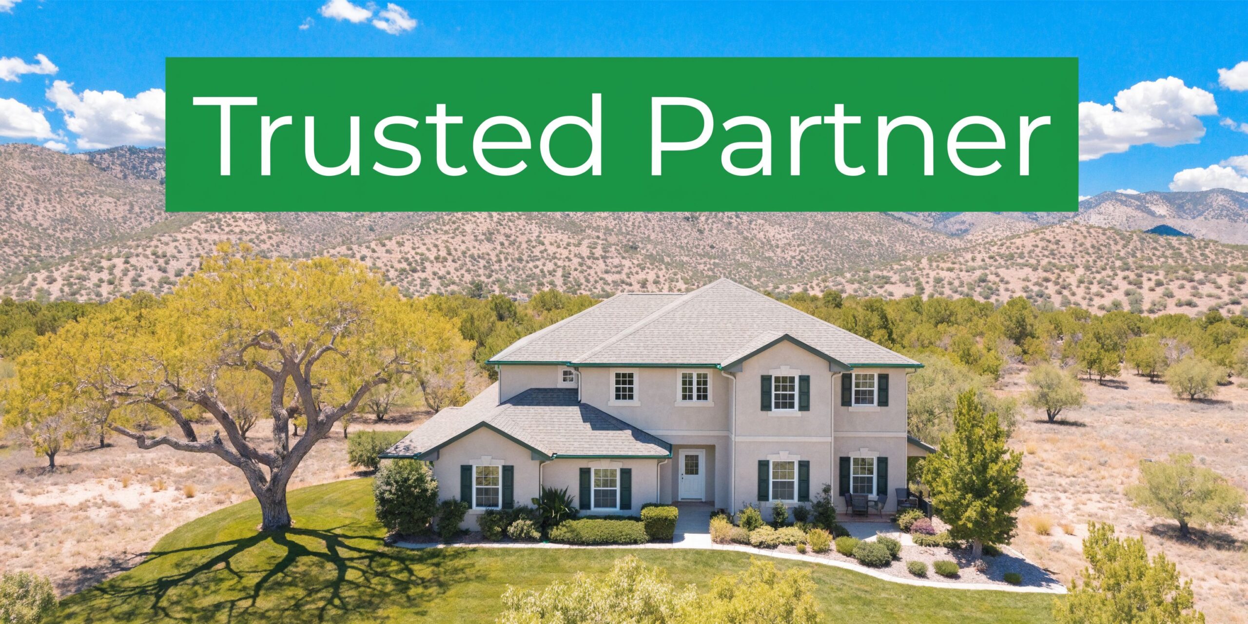 A large suburban home with a green roof and shutter details, surrounded by trees and mountains.