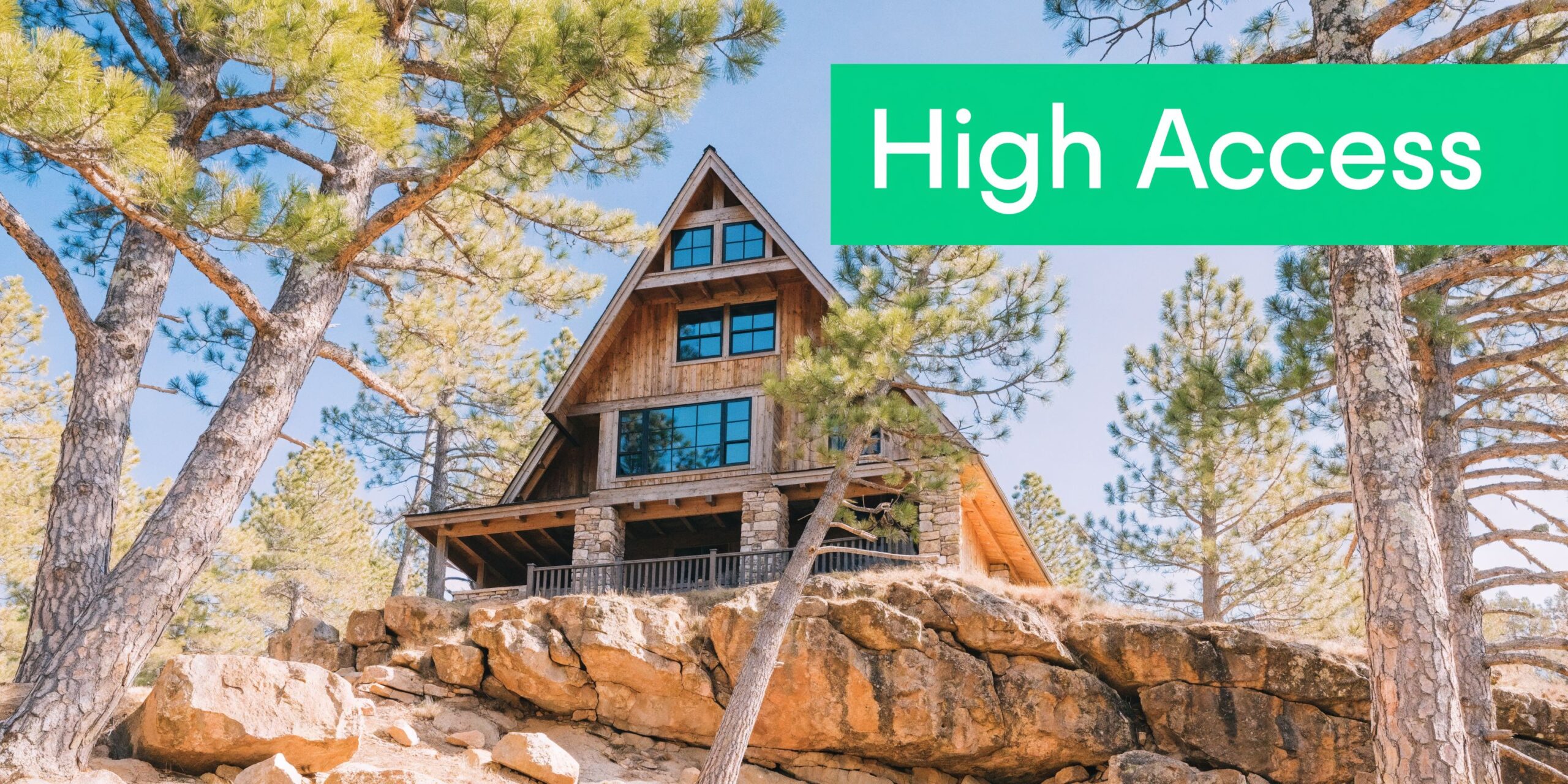 A large wooden A-frame cabin perched on a rocky cliff surrounded by tall pine trees.