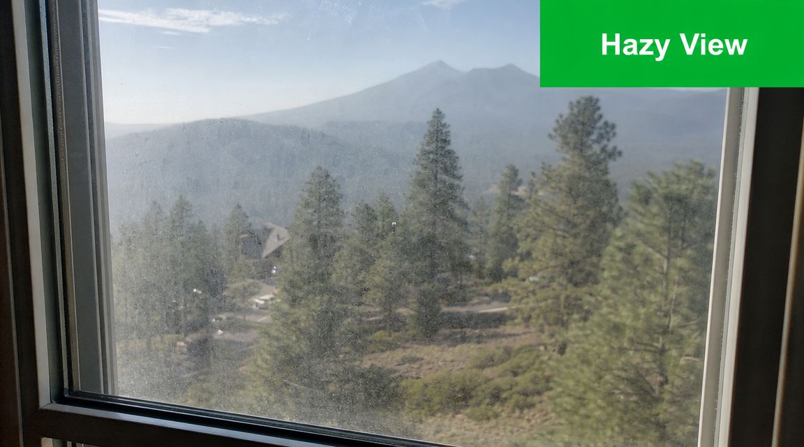 A hazy mountain view seen through a window covered in white water spots and streaks.