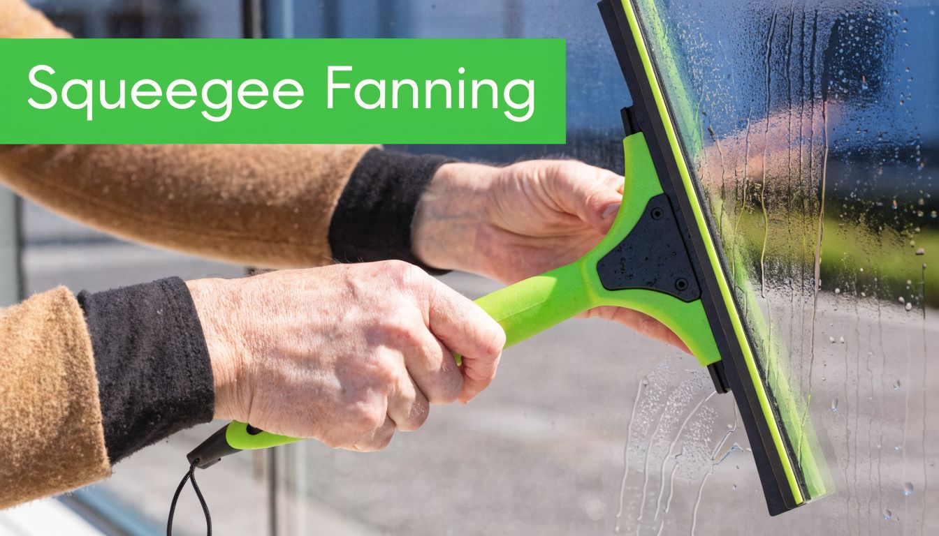 A close-up shot of a person using a green squeegee to clean a glass window.